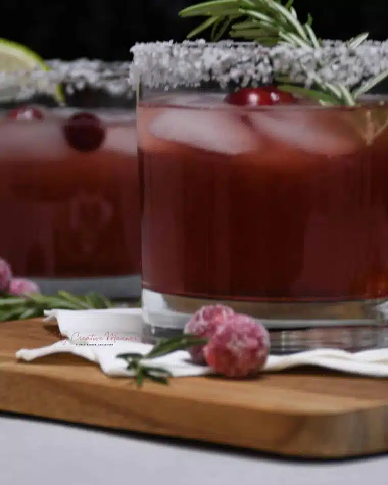 Cranberry margarita fills a cocktail glass that has been garnished with fresh cranberries and rosemary.