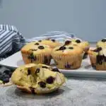 A close up of a blueberry almond muffin split in half with more muffins on a platter behind the the single muffin.