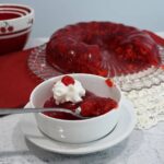 A bowl that has the cherry jello salad in it with more on a platter behind it.