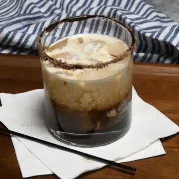 A cocktail glass that is rimmed with chocolate shaving with a chocolate white Russian drink in it.