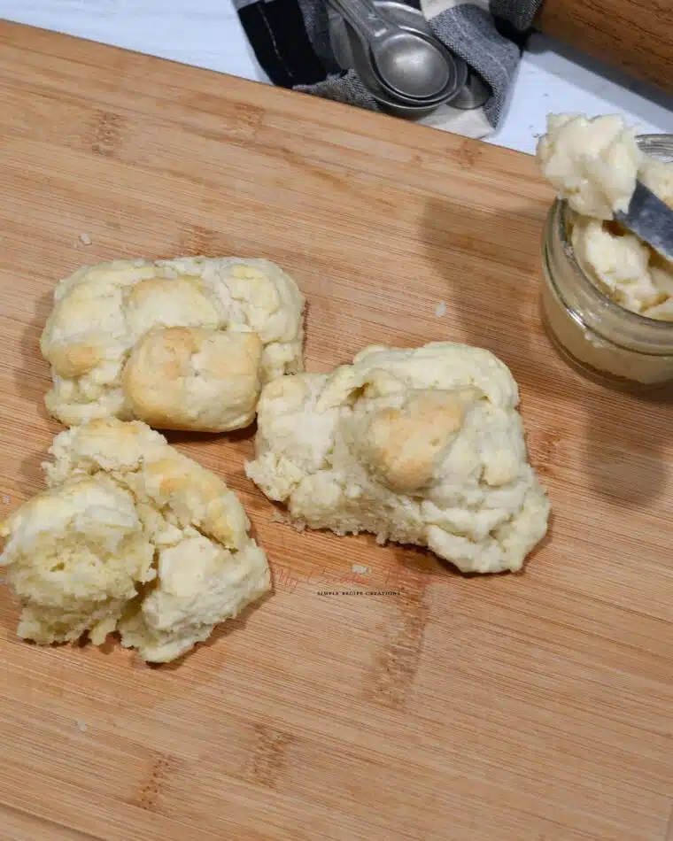 Overhead of three biscuits on a cutting board with a jar of butter next to them.