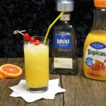 A cocktail glass that is filled with orange juice and tequila garnished with cherries.
