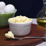 A close up of a knife that has the homemade avocado mayo on it with more of it in a bowl behind the knife.