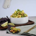 A blue torilla chip with the pineapple guacamole recipe on it. There is more of the sweet and spicy guacamole in a bowl.