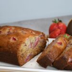 A loaf of fresh strawberry banana bread sliced on a platter.