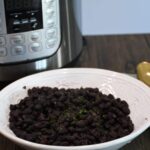A bowl filled with black bean and an Instant Pot that is behind the bowl.