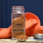 The front a spice that is labeled fajita seasoning with the jar and measuring spoon filled with the spice blend.