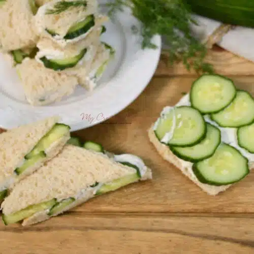 Looking down on a plate that has the cucumber cream cheese sandwiches and more of the sandwiches in front of the plate.