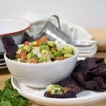 From view of a bowl filled with avocado and shrimp ceviche with blue tortilla chips.