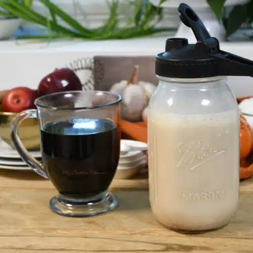 A cup of black coffee with a jar next to it that has the homemade pumpkin spice creamer in it.