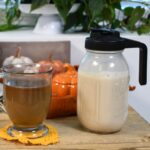 A mason jar that is filled with the homemade coffee cream that is pumpkin spice flavor.With a cup of coffee that has been mixed with the creamer.