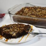 A slice of the German chocolate dump cake on a plate that has a fork with some of the gooey cake on it.